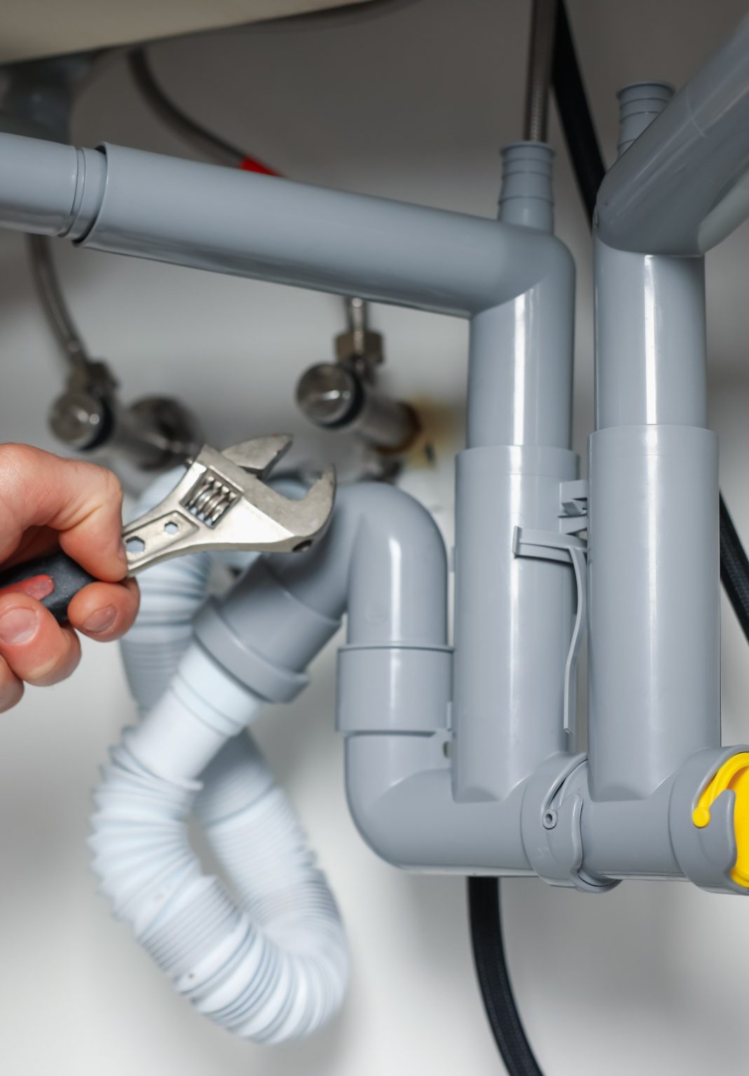 Hand tightening gray drain pipes under a sink with an adjustable wrench